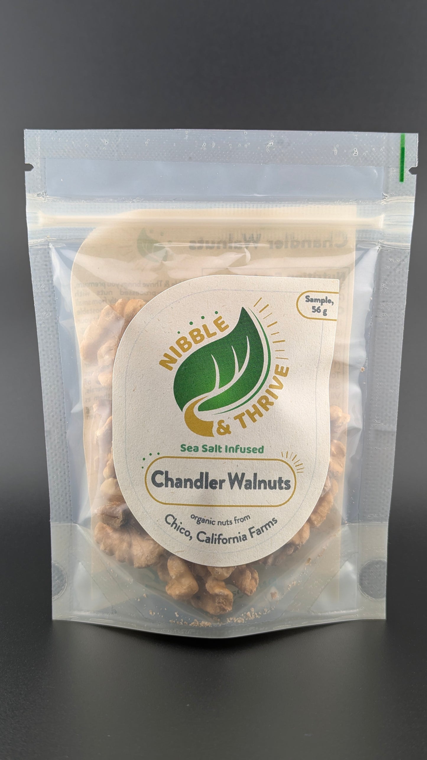 A clear, resealable bag of Infused Chandler Walnuts, Organic rests on a dark background. The label highlights these omega-3 rich walnuts as sea salt infused and organic from Chico, California Farms. The 56g sample size makes it perfect for trying this Walnut Clearance favorite.