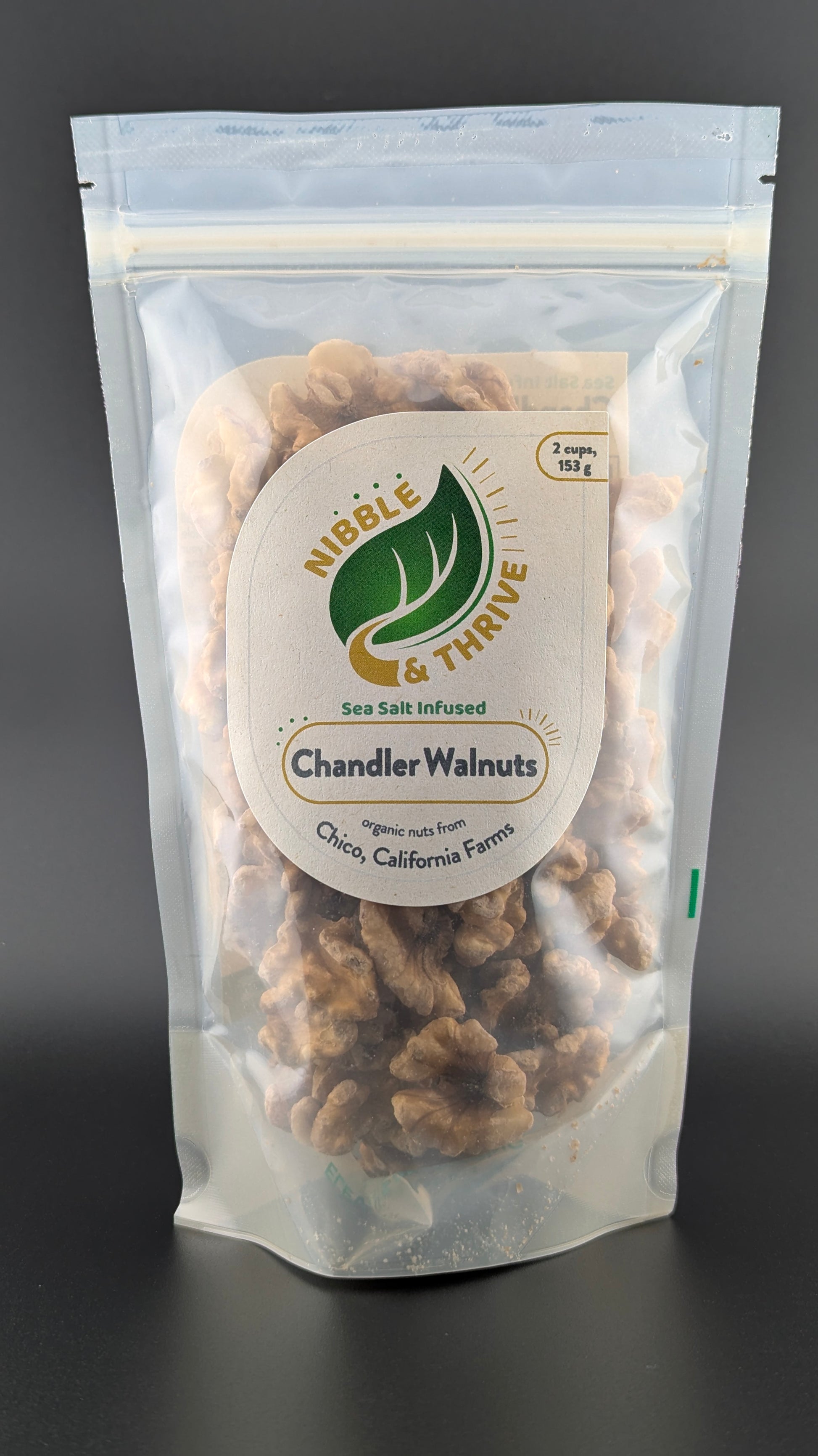 A 153g bag of Infused Chandler Walnuts, labeled Nibble & Thrive and Sea Salt Infused, contains organic walnuts rich in omega-3s sourced from Chico, California Farms. The bag is clear and resealable.