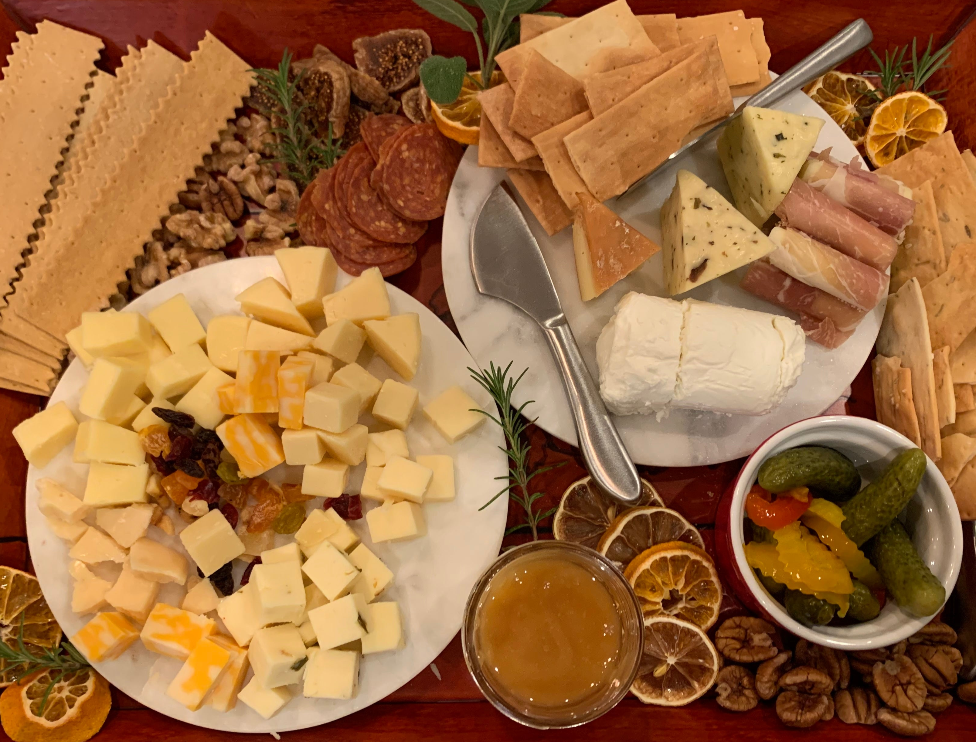 A charcuterie board filled with crackers, nuts, sliced figs, cubed cheeses, raisins and other dried fruits, salami, prosciutto, dried oranges, and fresh herbs!