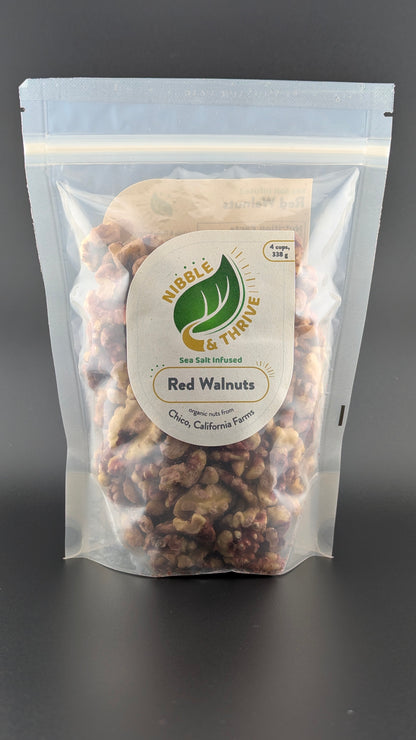 A sealed, transparent pouch labeled Nibble & Thrive features organic sea salt-infused red walnuts from Chico, California Farms with a green leaf graphic on a plain dark background.