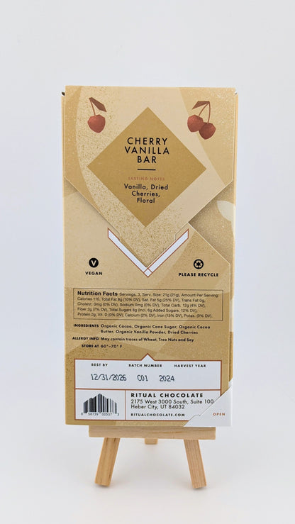 The Ritual Cherry Vanilla Bar 70% 2.12 oz combines Ritual Vanilla Chocolate with Montmorency cherries and floral notes. This vegan bar is presented on an easel and includes recycling symbols, nutrition facts, ingredients, and an expiration date of 12/31/2026.