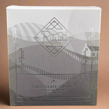 A 1 lb box of Ritual Chocolate Chunks - Chefs Blend 65% is crafted for home baking with organic cacao beans, featuring elegant geometric packaging and abstract illustrations of fields and hills.