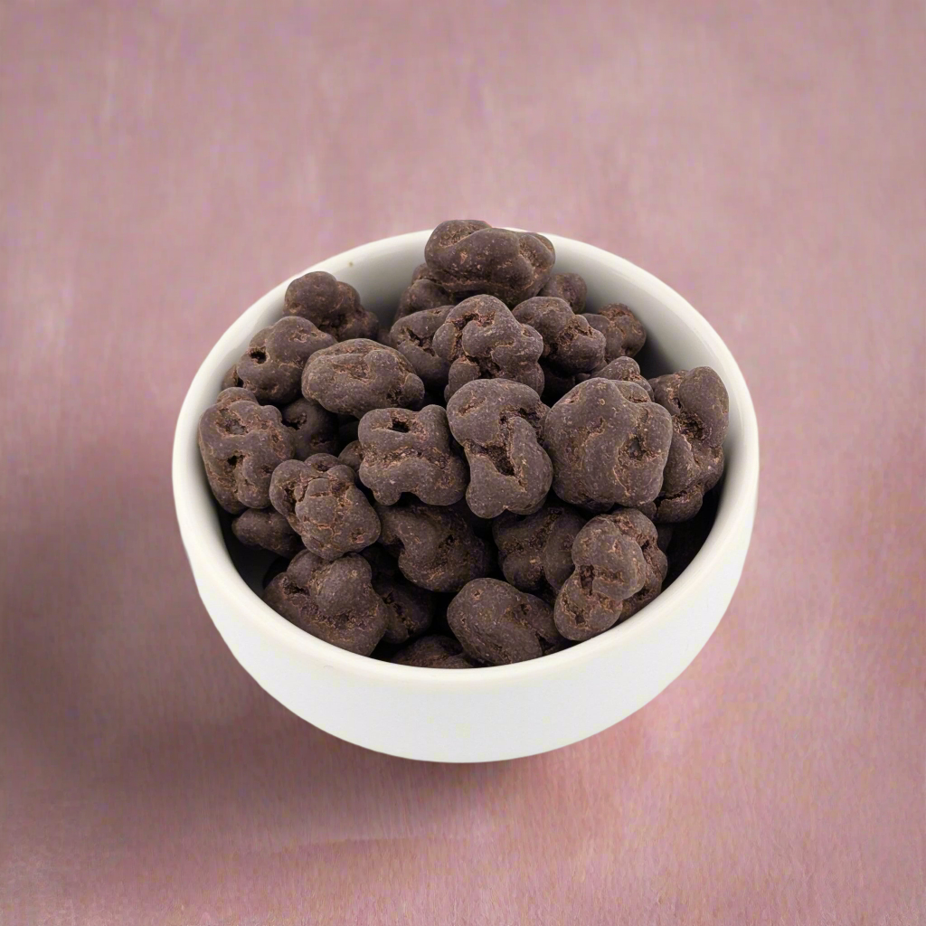 A white bowl filled with Ritual Vanilla Chocolate Cherries rests on a pinkish-brown surface.